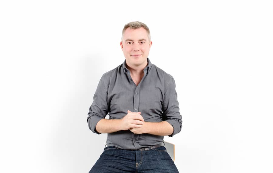 Peter Macleod sitting on a stool with his hands together in front of his stomach.