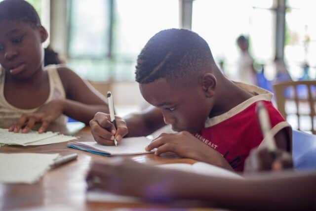 Young boy at school writing on a piece of paper with his head down.